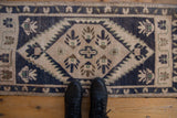 Distressed Oushak rug with dusty navy, antique ivory, bronze, and finned bud motifs.