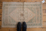Distressed vintage Oushak rug corner, featuring pale green border and intact selvage.