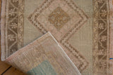 Distressed Oushak rug corner showing worn pile, visible foundation, and selvage.