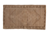 Distressed vintage Oushak mat featuring subtle diamond medallion on abrashed sand and beige field, 1'9