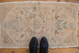Distressed Oushak rug mat with faded beige pile and turquoise and brown floral designs.
