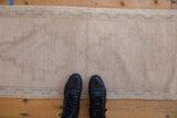 Textured distressed cream Oushak runner pile with subtle green border and black boots.