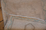 Distressed Oushak rug corner showing worn cream pile, intact selvage, and ocean green border.