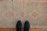 Distressed Oushak rug close-up: low pile, neutral beige, seafoam green, and hook and latch pattern.