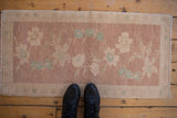 Vintage distressed Oushak mat with floral sprays in dusty mauve and seafoam, with feet for scale.