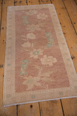 Angled perspective on a vintage distressed Oushak rug with a floral spray in mauve and seafoam green.