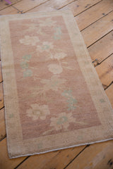 Angled view of a distressed Turkish Oushak mat with faded mauve and seafoam florals.