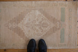 Vintage distressed Oushak rug in ivory, beige, and seafoam green, shown with boots for scale.