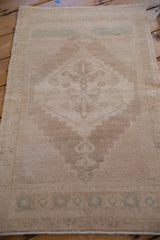 Distressed vintage Oushak rug close-up, showing faded geometric motifs in seafoam green on a beige field.
