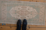 Black boots on a vintage distressed Oushak runner, showing faded seafoam green and sand tones.