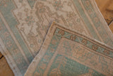 Distressed Oushak rug fold reveals seafoam, sand geometric vinery, foundation wear, and intact selvage.