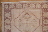 Distressed Oushak rug corner detail with ivory field, dusty copper palmette border, and visible pile wear.