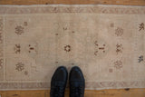 Distressed Oushak rug with faded beige field, coffee brown floral and stepped motifs.