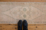 Distressed vintage Oushak runner rug, showcasing its muted ivory and seafoam green medallion pattern.
