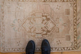 Distressed vintage Oushak rug mat in soft ivory and beige, black boots visible.