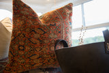 Close-up of vintage Persian rug fragment pillow showing textured rust coral and blue pattern.