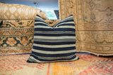Handwoven African textile pillow showcasing varied indigo and cream stripes.