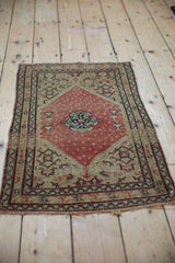 Angled view of an antique Persian Senneh rug, showcasing the Herati motif and faded red medallion.