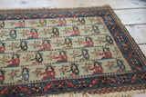 Angled view of vintage Persian pictorial rug, showing the floral border and tattered fringe.