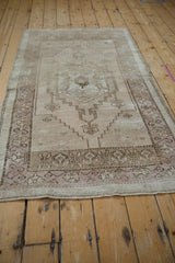 Distressed Oushak rug corner showing floral cross-sections in beige and mauve with secured fringe.