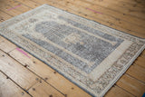 Angled view of a distressed vintage Sparta prayer rug in soft ivory and denim.