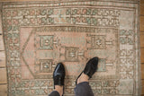 Distressed vintage Melas rug underfoot, showing short pile and geometric rose and seafoam motifs.