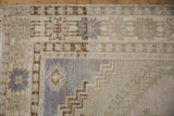 Distressed Oushak rug corner showing faded beige and dusty blue geometric patterns.