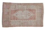 Vintage distressed Oushak rug with a faded central medallion in dusty terracotta, beige, and soft pink.