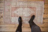 Small vintage Oushak rug with distressed texture and faded pink motifs, shown to scale from above.
