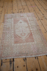 Angled view of a distressed vintage Oushak rug, showing its faded terracotta and ivory medallion design.