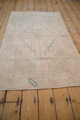 Distressed Oushak runner's pale rose and green geometric pile with subtle foundation exposure.