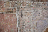 Distressed Oushak rug corner showing faded mauve pile and its hand-knotted foundation.