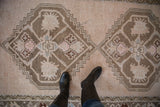 Distressed Oushak runner with an antique ivory and chestnut stylized geometric medallion.