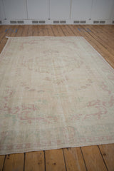 Worn ivory pile of a distressed Oushak rug with faded raspberry and mint green patterns.