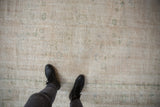 Distressed vintage Oushak rug showing worn texture, ivory ground, and subtle green motifs.