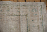 Distressed Oushak rug corner revealing worn platinum pile and geometric olive green border.