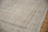 Distressed Oushak carpet with worn pile, geometric border, and muted ivory and sage tones.