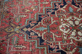 Vintage Heriz carpet's geometric vinery, stepped patterns, brick red, navy blue tones.