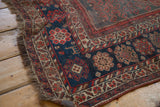 Rolled corner of a vintage Kamseh rug, showing madder red floral borders and indigo field.