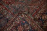 Folded vintage Kamseh rug, Herati field, madder red, navy blue floral border, and worn fringe.