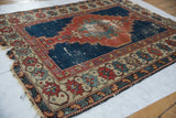 Tattered edge of antique Shirvan rug, showcasing interconnected red, blue, ivory floral border.