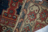 Worn pile and tattered edge of an antique Shirvan rug, revealing madder red and ivory patterns.