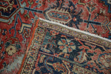 Vintage Heriz carpet close-up with worn red, navy, blue floral patterns and visible foundation.