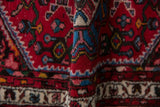 Close-up of folded hand-knotted Borchalou rug: brick red, sapphire blue, pearl border motif.