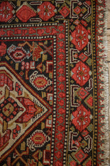 Malayer runner detail: cherry red floral pomegranate border, navy field motifs, and worn fringe.