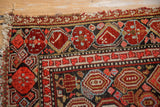 Vintage Malayer rug runner corner with aged fringe, revealing cherry red, navy, and gold geometric floral patterns.