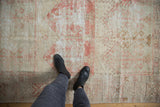 Faded raspberry red geometric plant motifs on the worn ivory pile of a vintage Oushak rug.