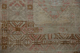Distressed Oushak rug close-up: worn pile with pale raspberry and brown geometric patterns.