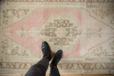 Standing perspective over a distressed Oushak rug with a soft pink and beige geometric pattern.