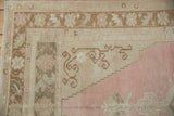 Hook and latch motifs bordering the abrashed pink field on a distressed vintage Turkish rug.